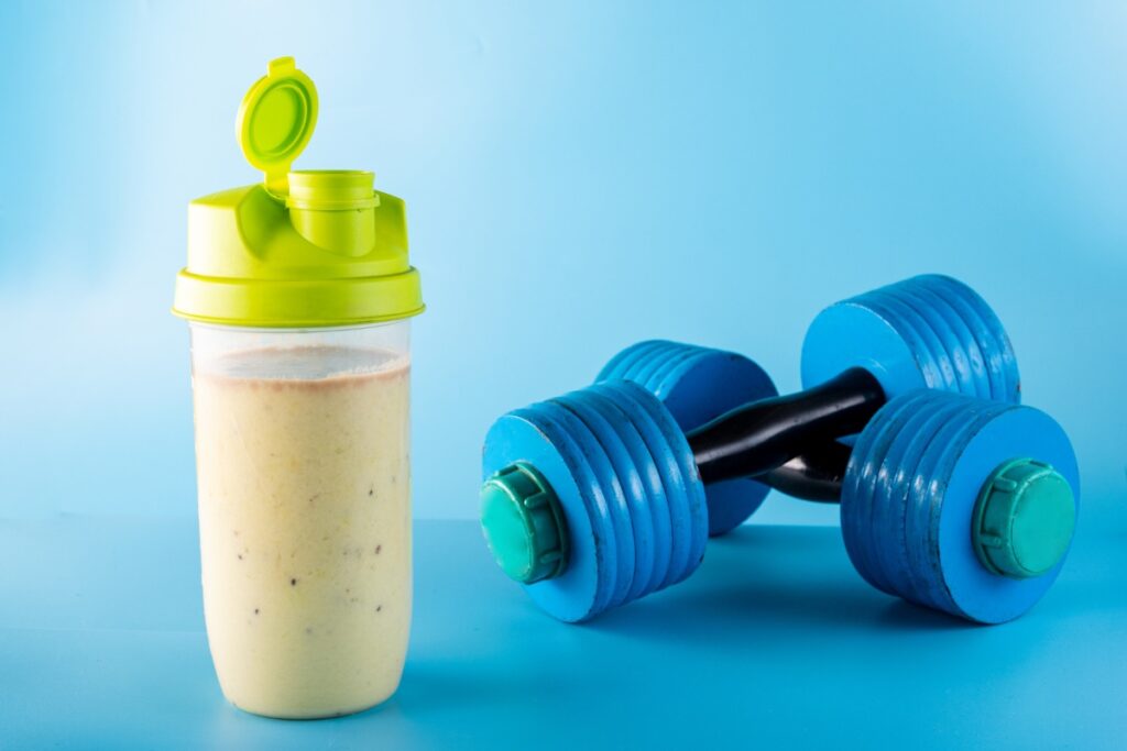 Protéine pour Masse Musculaire : Shaker rempli d'un shake protéiné crémeux avec des haltères en arrière-plan